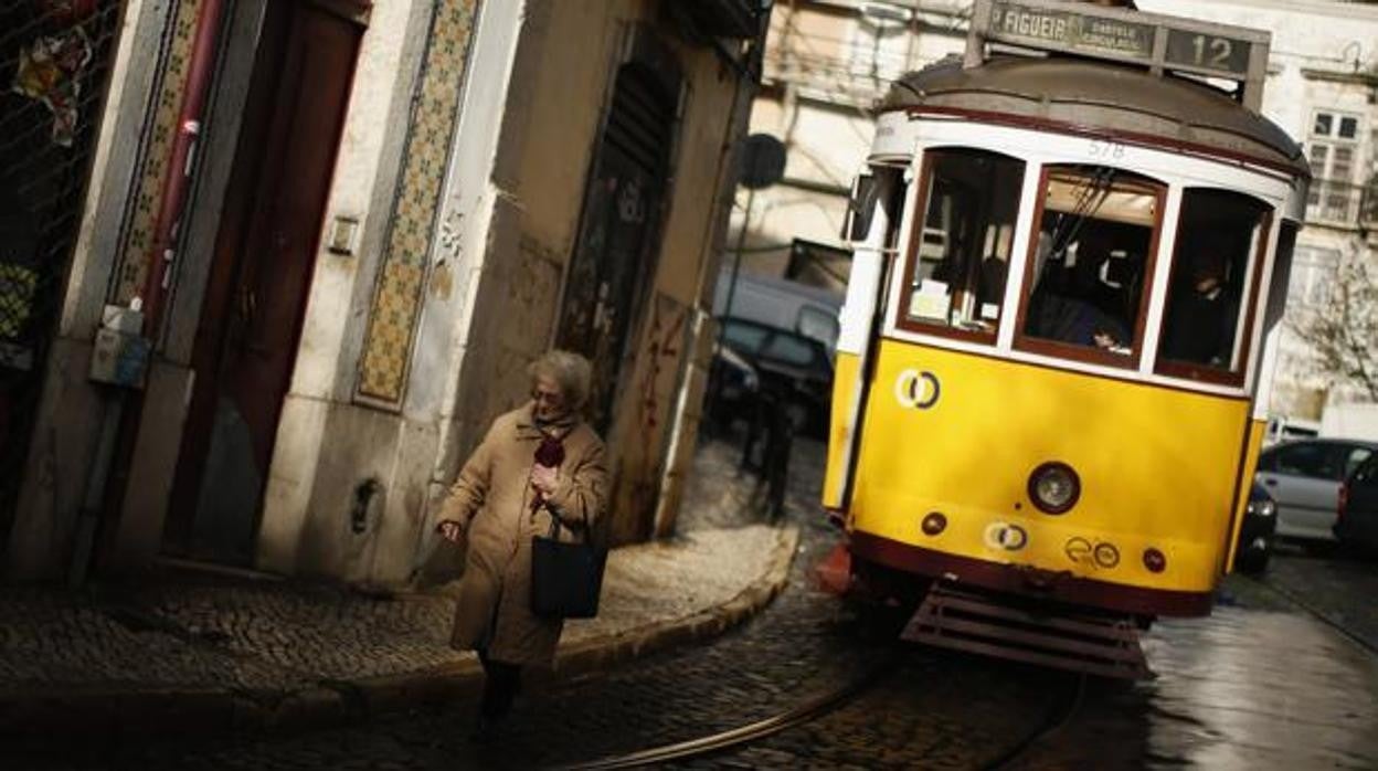 Una mujer pasea por el barrio de la Alfama, junto a uno de los típicos tranvías de Lisboa