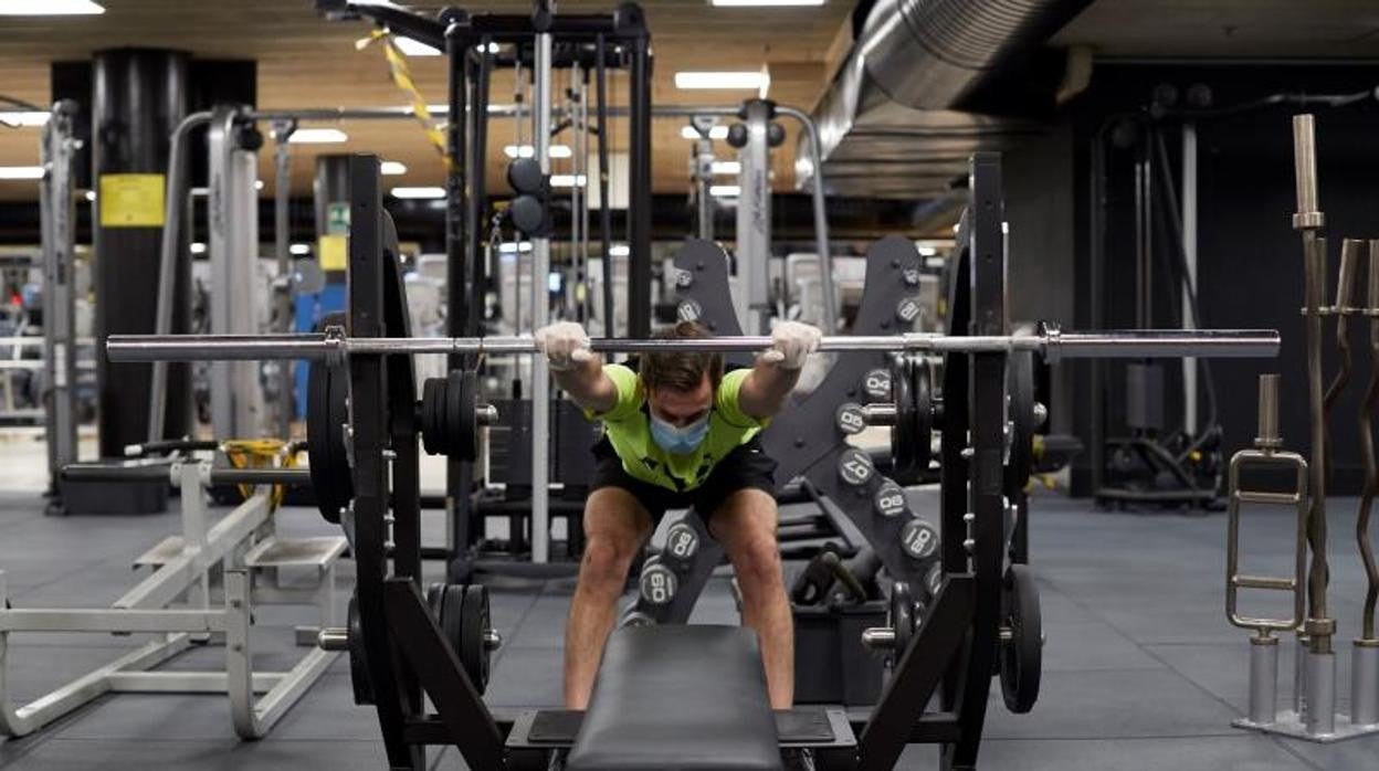 Un usuario se ejercita con la barra de pesas en un gimnasio