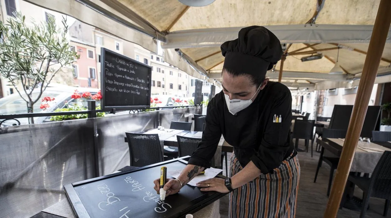 Una camarera prepara todo para acoger a clientes, que se sienten a comer en la terraza en esta fase de la emergencia, en la que el país reclama el pase sanitario en los hoteles, hostales y restaurantes