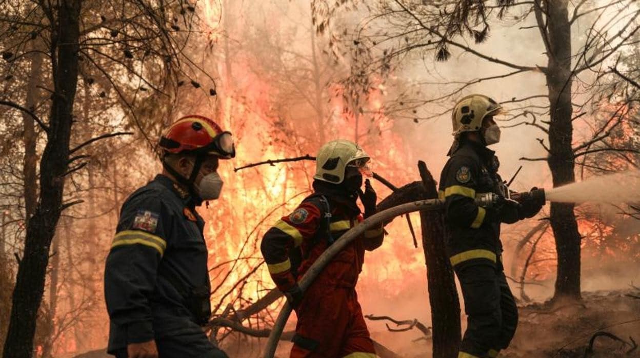 Dos bomberos de Grecia y uno de Eslovaquia intentan extinguir un incendio forestal en la aldea de Avgaria, en la isla de Evia, Grecia