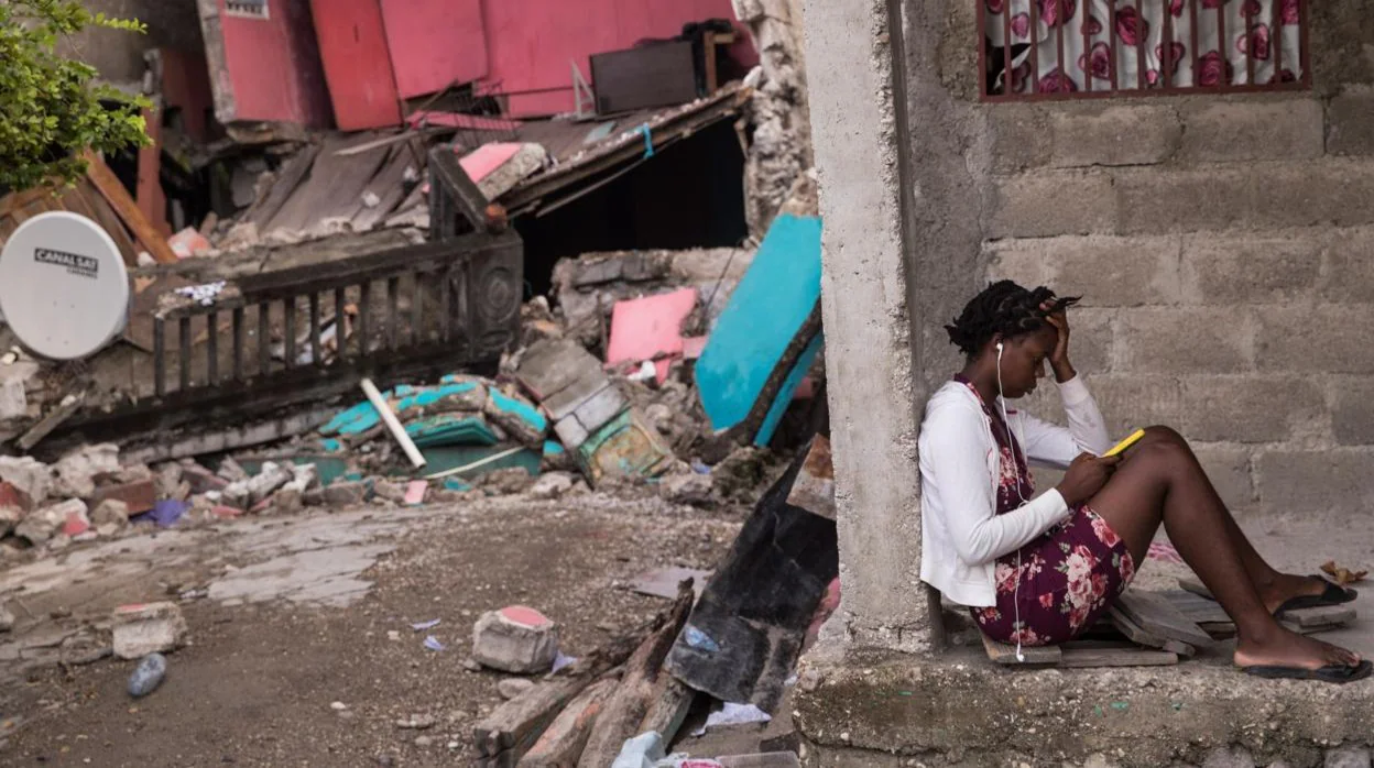 Una joven revisa su teléfono junto a su hogar afectado por el terremoto, hoy en Les Cayes (Haití)