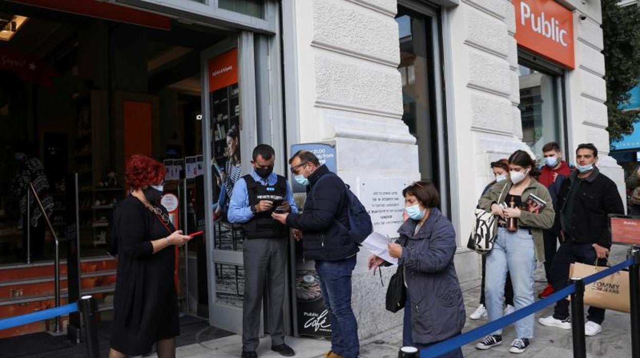 Varios griegos enseñan el pasaporte Covid antes de entrar en una tienda, en Atenas