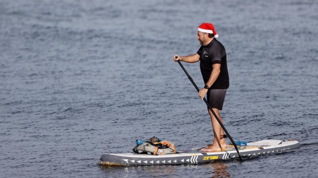 Una persona ataviada con un gorro de Papá Noel practica paddle surf en las aguas de la Malvarrosa