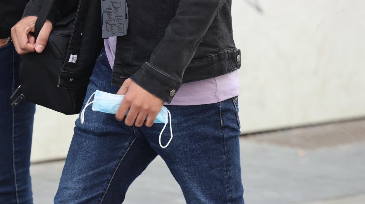 Un chico pasea con una mascarilla quirúrgica en la mano