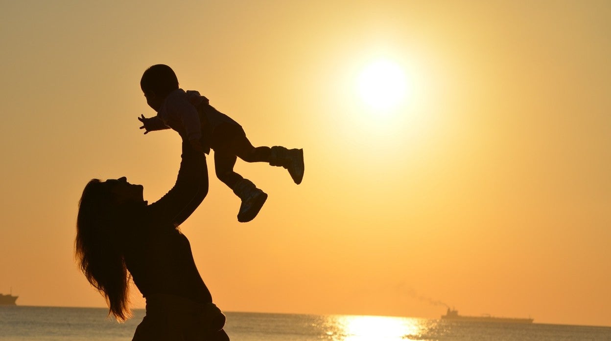 Una mujer coge a su hijo frente a la playa