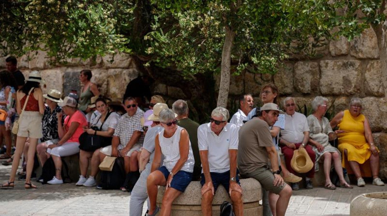 Unos turistas descansan sentados a la sombra junto a los Reales Alcázares de Sevilla