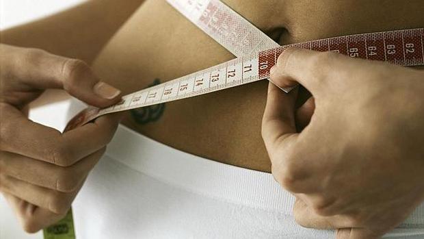 Una mujer muestra mide su talla con un metro