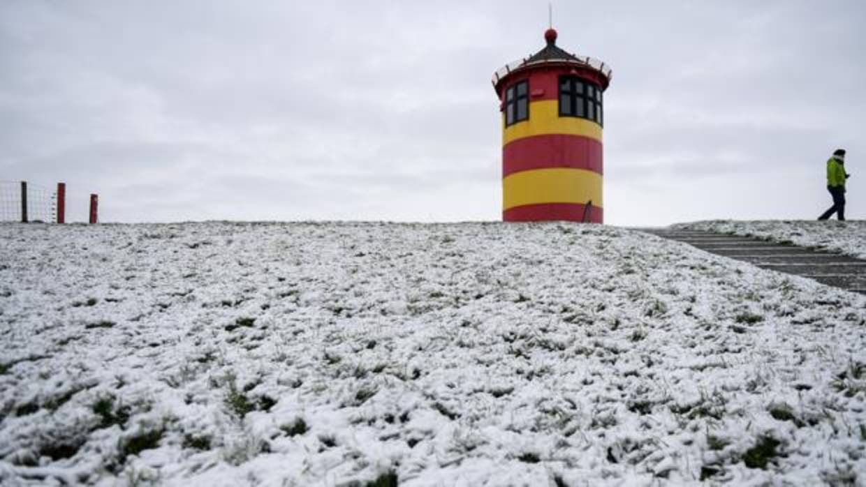 Una mujer camina por un paisaje nevado junto al faro de Pilsum (Alemania). El fuerte temporal de vientos, lluvia y nieve que afecta a media Europa ha obligado a cancelar vuelos y emitir avisos de alerta en varios países del continente,