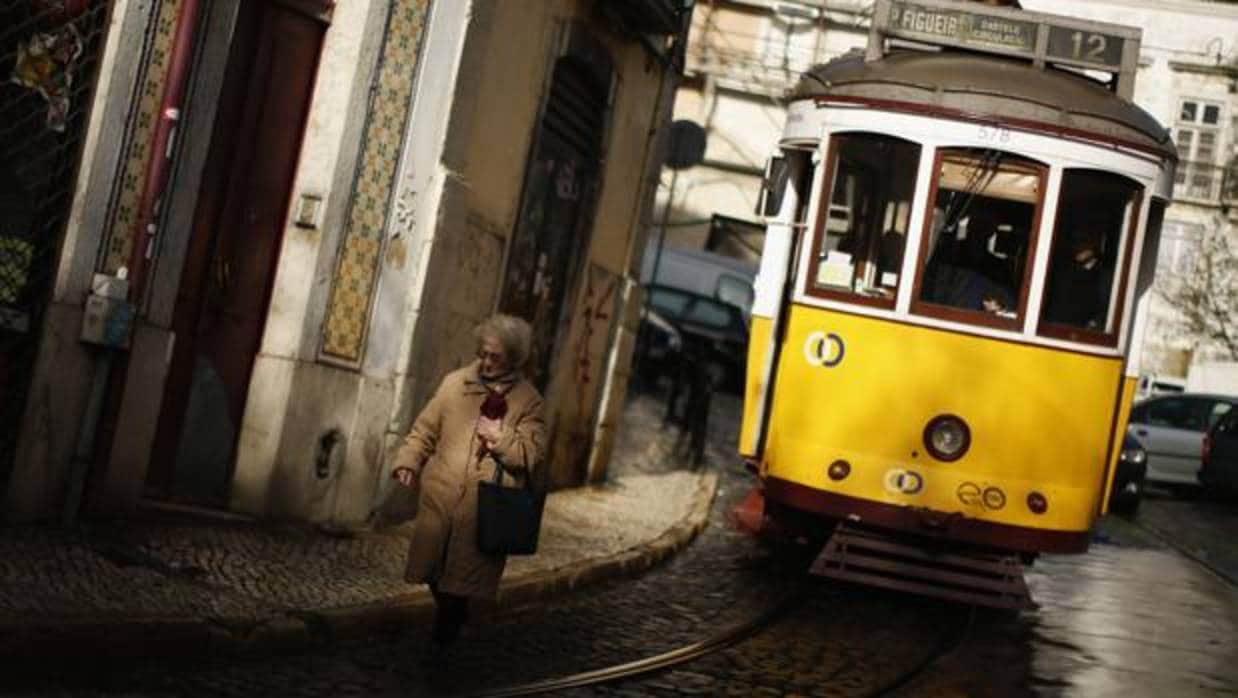 Una mujer pasea por el barrio de la Alfama, junto a uno de los típicos tranvías de Lisboa
