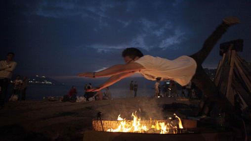 Un joven salta una pequeña hoguera en la playa del Orzán, en La Coruña, durante la celebración de la gran fiesta del fuego de San Juan